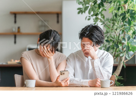 家でスマートフォンを見ながら落ち込む夫婦・カップル（ニュース・投資・株） 121986626