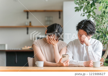 家でスマートフォンを見ながら落ち込む夫婦・カップル（ニュース・投資・株） 121986627