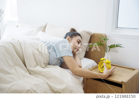 Asian women sleep wake up in white cozy bedroom happy time morning sunrise. Beautiful chinese use hand stop time alarm clock. Happy person lifestyle wake up in morning wellbeing relax sleepy napping 121988150