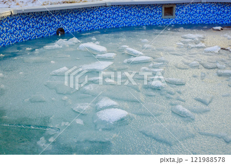 Ice forms on surface of pool, creating wintery atmosphere with blue tiles contrasting frozen water. 121988578