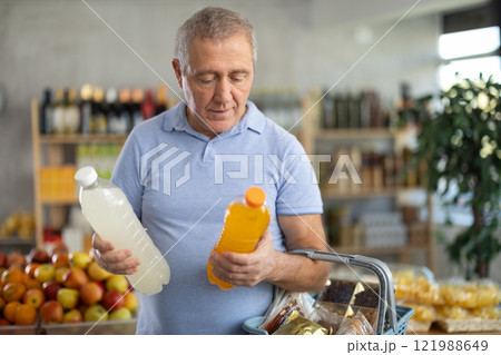 Mature man hold white plastic bottles and choose consider drink in store Mature man hold white plastic bottles and choose consider drink in store 121988649