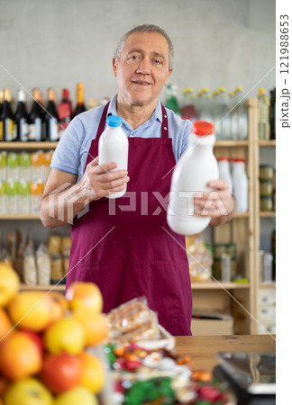Elderly man seller offers milk in grocery store Elderly man seller offers milk in grocery store 121988653