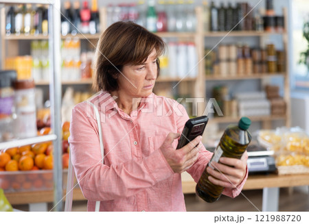 Mature woman is scanning QR on a bottle of olive oil in grocery 121988720
