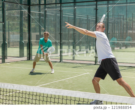 Four men practice playing padel on an outdoor court 121988854