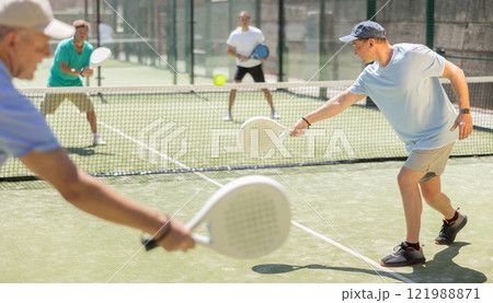 Adult and elderly men playing padel against two men Adult and elderly men playing padel against two men 121988871