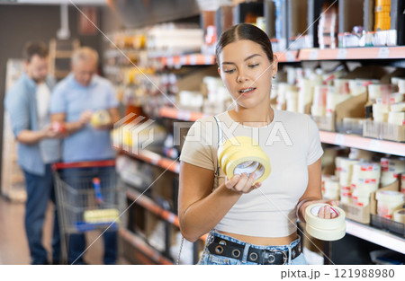 Young woman buy sticky adhesive tape in construction store for carrying out internal finishing work Young woman buy sticky adhesive tape in construction store for carrying out internal finishing work 121988980