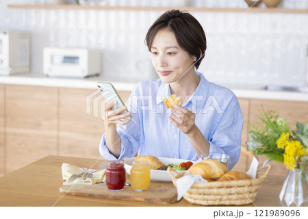 スマホを見ながら朝食を食べる女性 スマホを見ながら朝食を食べる女性 121989096