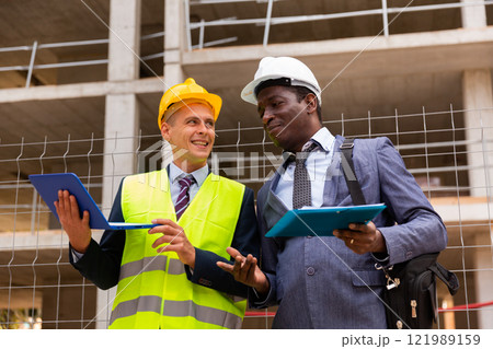 Head of construction and representative of developer are discussing documents and drawings at construction site 121989159
