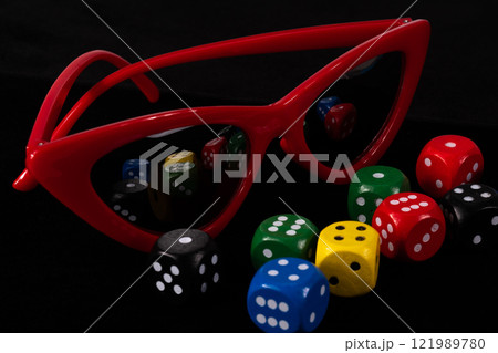 Red cat eye sunglasses and dice cubes on black background nearby. High quality photo 121989780