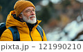 An elderly man enjoys a moment outdoors while wearing a vibrant yellow jacket and beanie. He gazes thoughtfully into the distance. Perfect for travel and lifestyle themes. AI 121990210