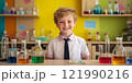 A cheerful boy smiles while sitting at a table filled with colorful science beakers and flasks. The background is vibrant and playful. Perfect for educational or fun themes. AI 121990216