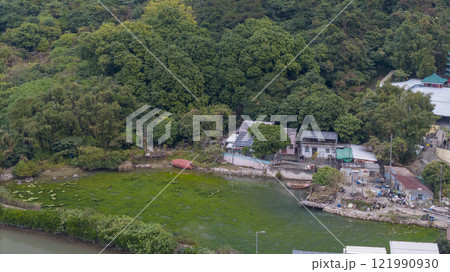 landscape of trees, a tranquil pond, and a village next to a lush hillside. Tai O Dec 31 2024 121990930