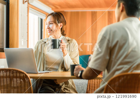 家・別荘・コテージでパソコンをやりながらコーヒーを飲む夫婦・カップル・男女(話す・会話) 121991690