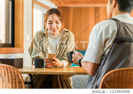 家・別荘・コテージでスマホを見ながらコーヒーを飲む夫婦・カップル・男女(話す・会話) 家・別荘・コテージでスマホを見ながらコーヒーを飲む夫婦・カップル・男女(話す・会話) 121991699