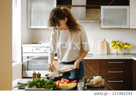 Woman pouring grated cheese into a bowl 121992291