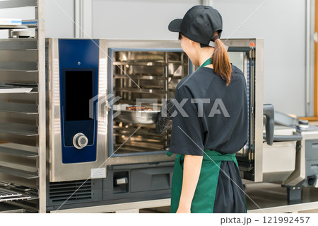 厨房でスチームオーブンを使う調理スタッフの女性 121992457