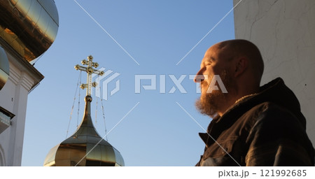Bearded man performs sign of cross with Orthodox church domes in background, emphasizing spirituality, sacred rituals, and cultural heritage in a tranquil religious setting. Man crossing himself Bearded man performs sign of cross with Orthodox church domes in background, emphasizing spirituality, sacred rituals, and cultural heritage in a tranquil religious setting. Man crossing himself 121992685