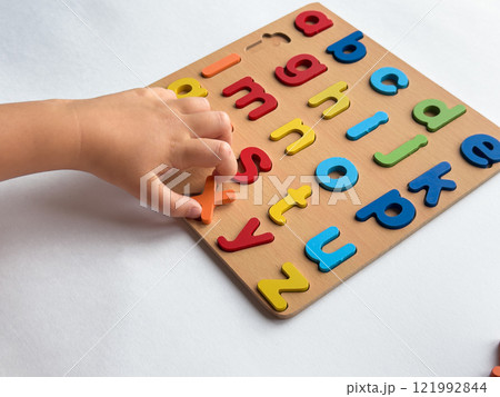 Childs hand arranging colorful alphabet puzzle on wooden board Childs hand arranging colorful alphabet puzzle on wooden board 121992844