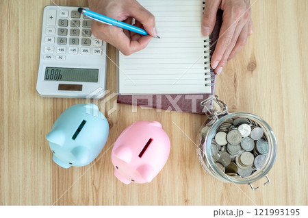 Cropped shot view of someone try to counting saving money by calculator and write it on book. Cropped shot view of someone try to counting saving money by calculator and write it on book. 121993195