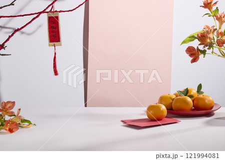 A Chinese New Year display includes a pink panel on a white backdrop, tangerines and alstroemeria flowers on fortunate envelopes, a red branch hanging calligraphists, and an empty products display. 121994081