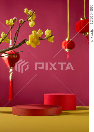Concept for the Lunar New Year. Frontal view of a crimson background and an empty red cylindrical pedestal for displaying product. Decorated with Chinese lanterns in red and yellow apricot blooms. Concept for the Lunar New Year. Frontal view of a crimson background and an empty red cylindrical pedestal for displaying product. Decorated with Chinese lanterns in red and yellow apricot blooms. 121994090