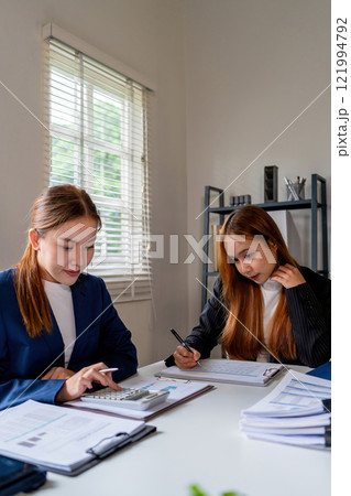 Businesswoman sitting at desk on couch in workplace or at home working on laptop and analyzing data on charts and graphs and writing on papers to make business plan and strategies for company 121994792