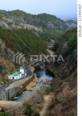 極寒の奈良布目ダム鉛色の空から陽春まで　ダム放水路にある水力発電所と谷間を流れる布目川 121995407