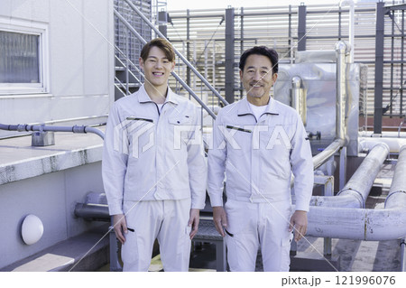 屋上の給排水設備の前に立つ作業服の男性2人　撮影協力：学校法人電波学園 東京電子專門学校 121996076
