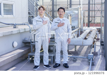 屋上の給排水設備の前に立つ作業服の男性2人　撮影協力：学校法人電波学園 東京電子專門学校 121996078