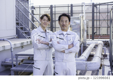 屋上の給排水設備の前に立つ作業服の男性2人　撮影協力：学校法人電波学園 東京電子專門学校 121996081