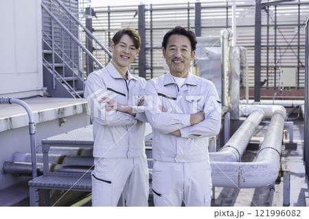 屋上の給排水設備の前に立つ作業服の男性2人　撮影協力：学校法人電波学園 東京電子專門学校 121996082