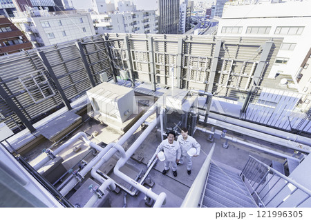 屋上の給排水設備の前に立つ作業服の男性2人　撮影協力：学校法人電波学園 東京電子專門学校 121996305