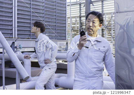 屋上の給排水設備の前でトランシーバーで話す作業服の男性 撮影協力:学校法人電波学園 東京電子專門学校 屋上の給排水設備の前でトランシーバーで話す作業服の男性 撮影協力:学校法人電波学園 東京電子專門学校 121996347