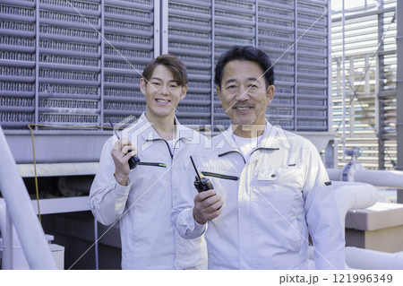 屋上の給排水設備の前でトランシーバーで話す作業服の男性 撮影協力:学校法人電波学園 東京電子專門学校 屋上の給排水設備の前でトランシーバーで話す作業服の男性 撮影協力:学校法人電波学園 東京電子專門学校 121996349