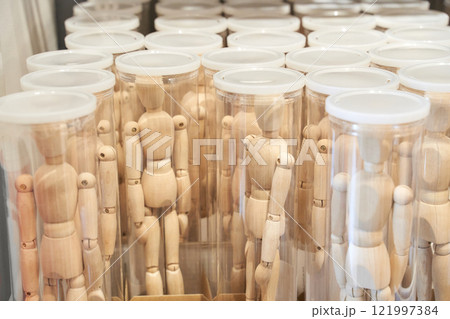 Wooden art mannequins standing in transparent cylindrical containers 121997384