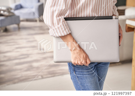 Caucasian female young adult holding laptop in modern living room setting Caucasian female young adult holding laptop in modern living room setting 121997397