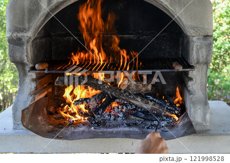 Hand keeps fire going in a grill with fiery flames - an empty fire grate 121998528