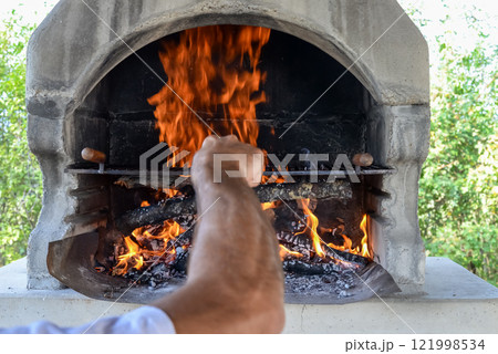 Hand keeps fire going in a grill with fiery flames - an empty fire grate Hand keeps fire going in a grill with fiery flames - an empty fire grate 121998534