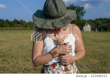 Woman with a summer hat holding a small yellow kitten in the countryside, in summertime Woman with a summer hat holding a small yellow kitten in the countryside, in summertime 121998552