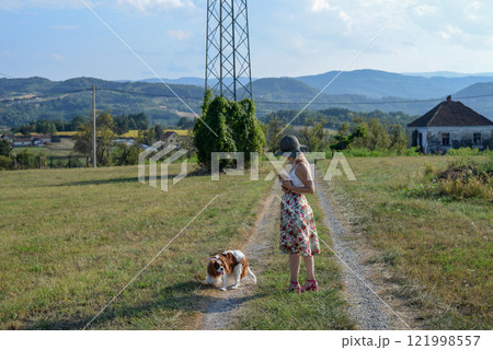Woman with a dog holds a little yellow kitten on a country road, in summer Woman with a dog holds a little yellow kitten on a country road, in summer 121998557