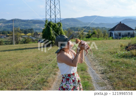 Woman with a hat is holding a small yellow kitten in the countryside, in summertime - exclusively reserved for real pet lovers 121998558