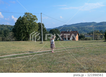 Woman with a summer hat is watching a countryside landscape in summertime Woman with a summer hat is watching a countryside landscape in summertime 121998561