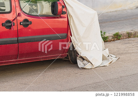 Red minivan after car accident with frontal impact is parked near sidewalk in street, covered with awning so not to spoil city landscape. Consequences of collision, costs, damage, insurance indemnity 121998858
