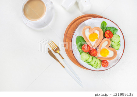 Breakfast on Valentine's Day fried eggs sausages in the shape of a heart and cup of coffee on a white background top view. copy space 121999138