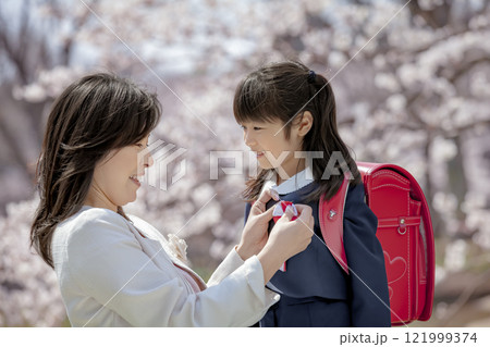 桜の咲く公園でランドセル姿の娘にリボンをつける母親 121999374
