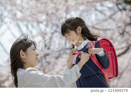 桜の咲く公園でランドセル姿の娘にリボンをつける母親 121999379