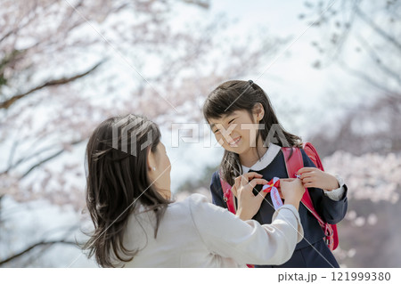 桜の咲く公園でランドセル姿の娘にリボンをつける母親 桜の咲く公園でランドセル姿の娘にリボンをつける母親 121999380