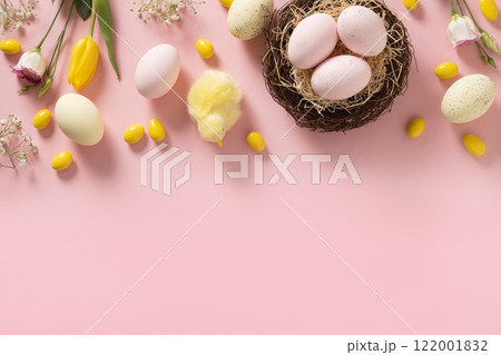 Easter frame with pastel chocolate candy sweets, eggs, flowers, decorative nest, gypsophila and yellow chick on pink background. View from above. Flat lay. Happy Easter greeting card. Copy space. 122001832