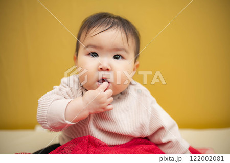 黄色バックでお座りしている涙目の赤ちゃん 黄色バックでお座りしている涙目の赤ちゃん 122002081