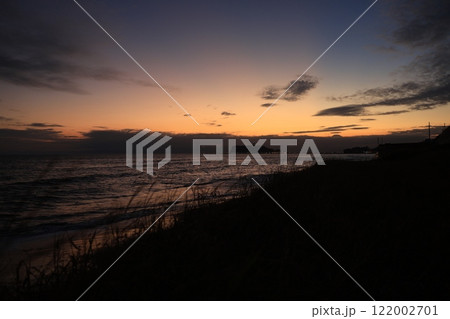 鎌倉・七里ヶ浜海岸から見る江ノ島とオレンジ色になる夕陽とのある風景 夕景 鎌倉・七里ヶ浜海岸から見る江ノ島とオレンジ色になる夕陽とのある風景 夕景 122002701
